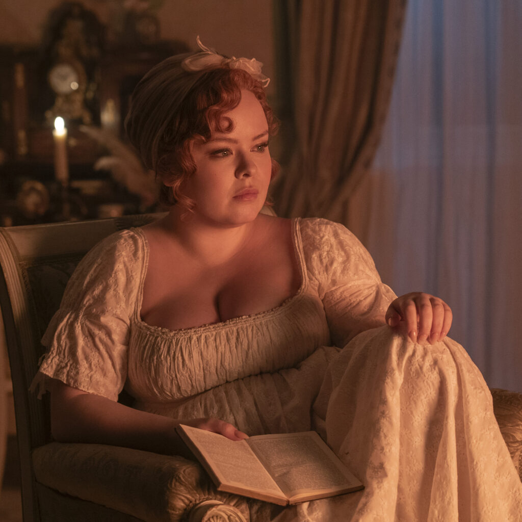 Nicola Coughlan as Penelope Featherington gazes at the fireplace while sitting in her nightgown. 